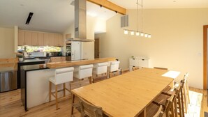 Una cocina moderna con armarios de madera, una isla central con taburetes de bar y una gran mesa de comedor.