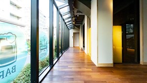 A corridor with wooden flooring, large windows, and a glass door leading to a room.