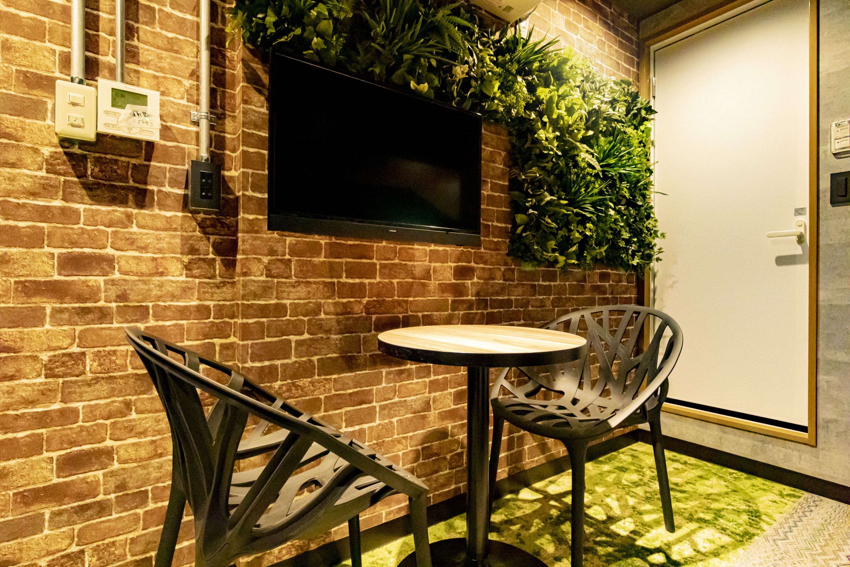 A brick wall with a flat-screen TV, a small table, and two chairs.