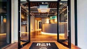 A hotel reception area with a modern design, including a reception desk, a digital display, and a black mat with the hotel name.
