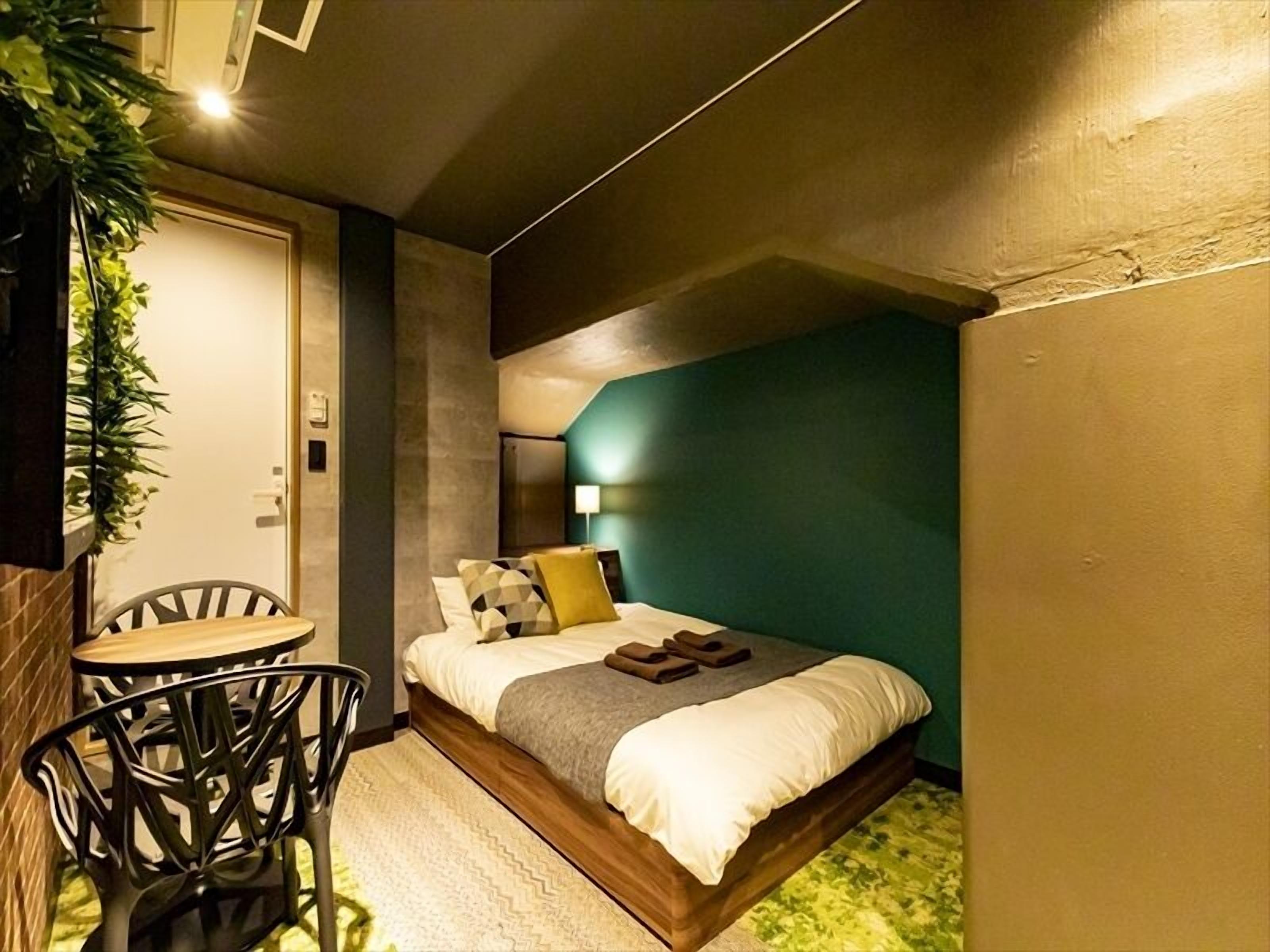 Een kleine kamer met een bed, een tafeltje en stoelen.