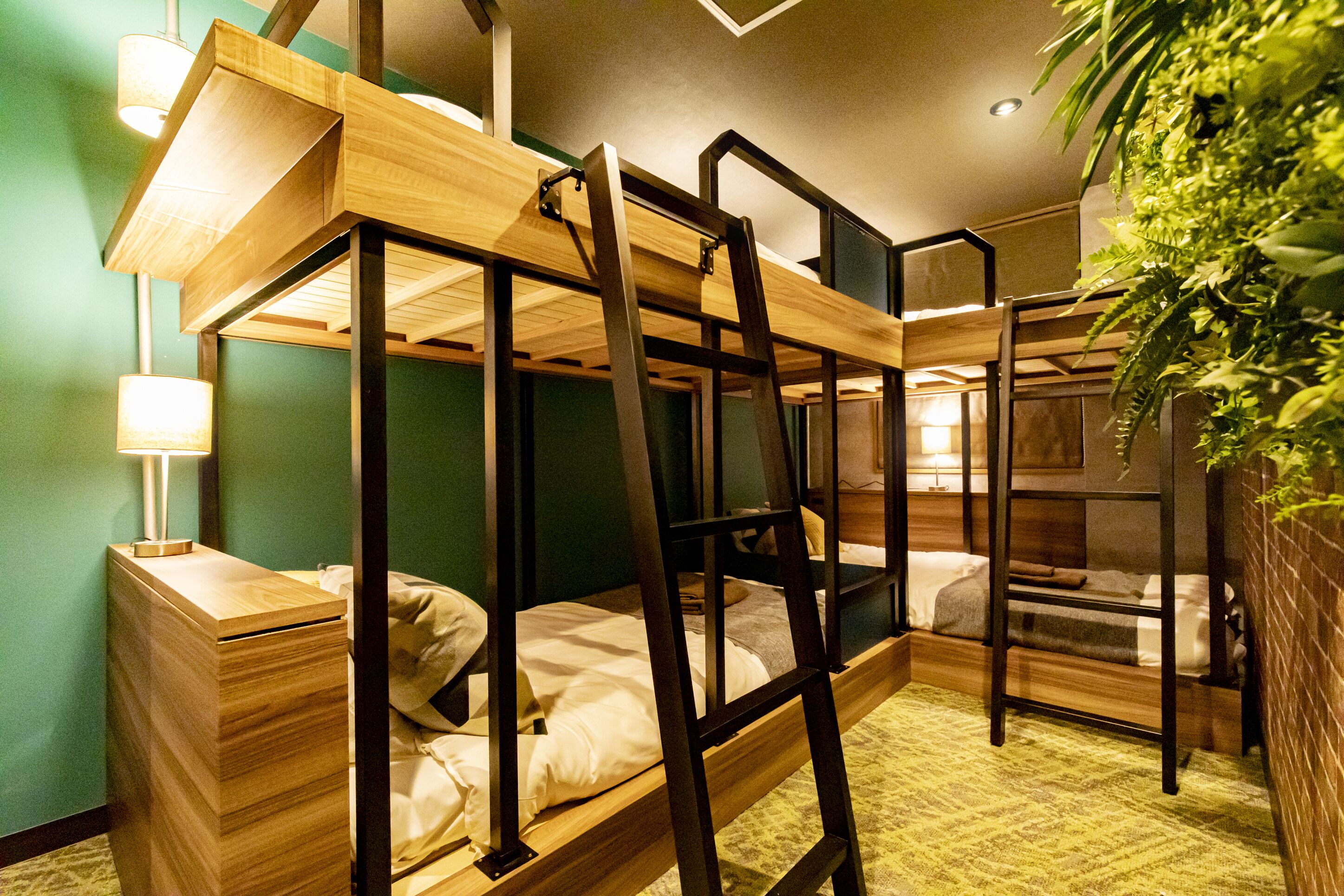 Habitación con literas, una escalera de madera, una mesita de noche con lámpara y pared verde.