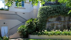 A courtyard with a stone wall, a metal staircase, and lush greenery.