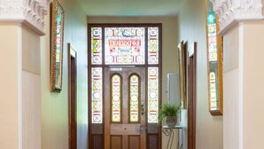 A hallway with a red carpet leading to a door with stained glass windows.