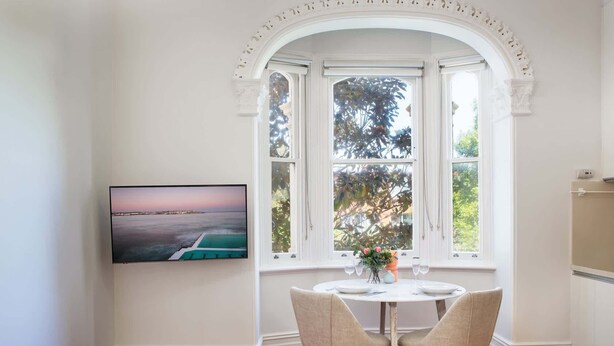 A dining area with a bay window, a television mounted on the wall, and a table set for two.