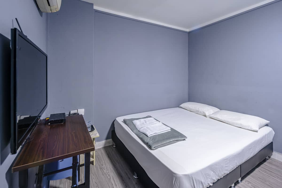 A bedroom with a bed, a desk, and a flat-screen TV.