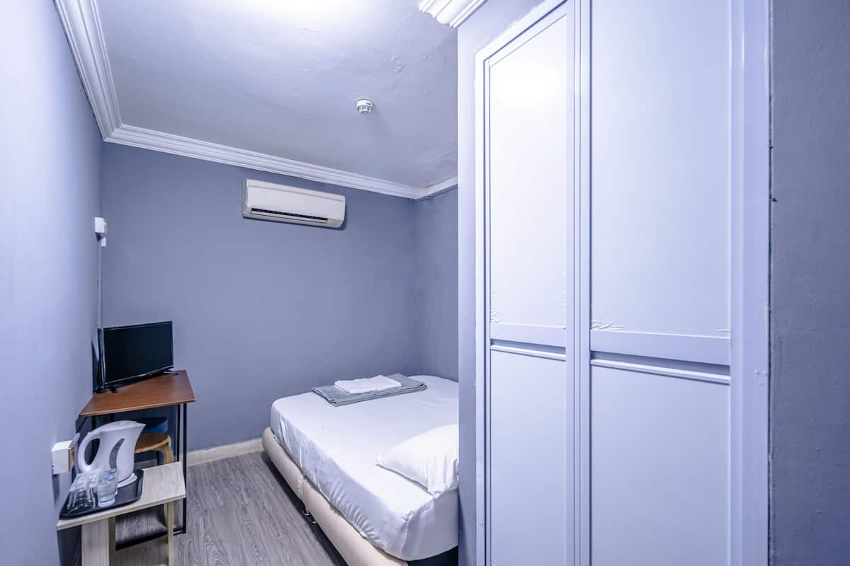 A small, neatly organized bedroom with a single bed, a desk with a computer, and a wardrobe.