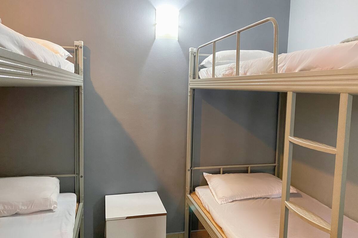 A bunk bed room with a small bedside table and a window.