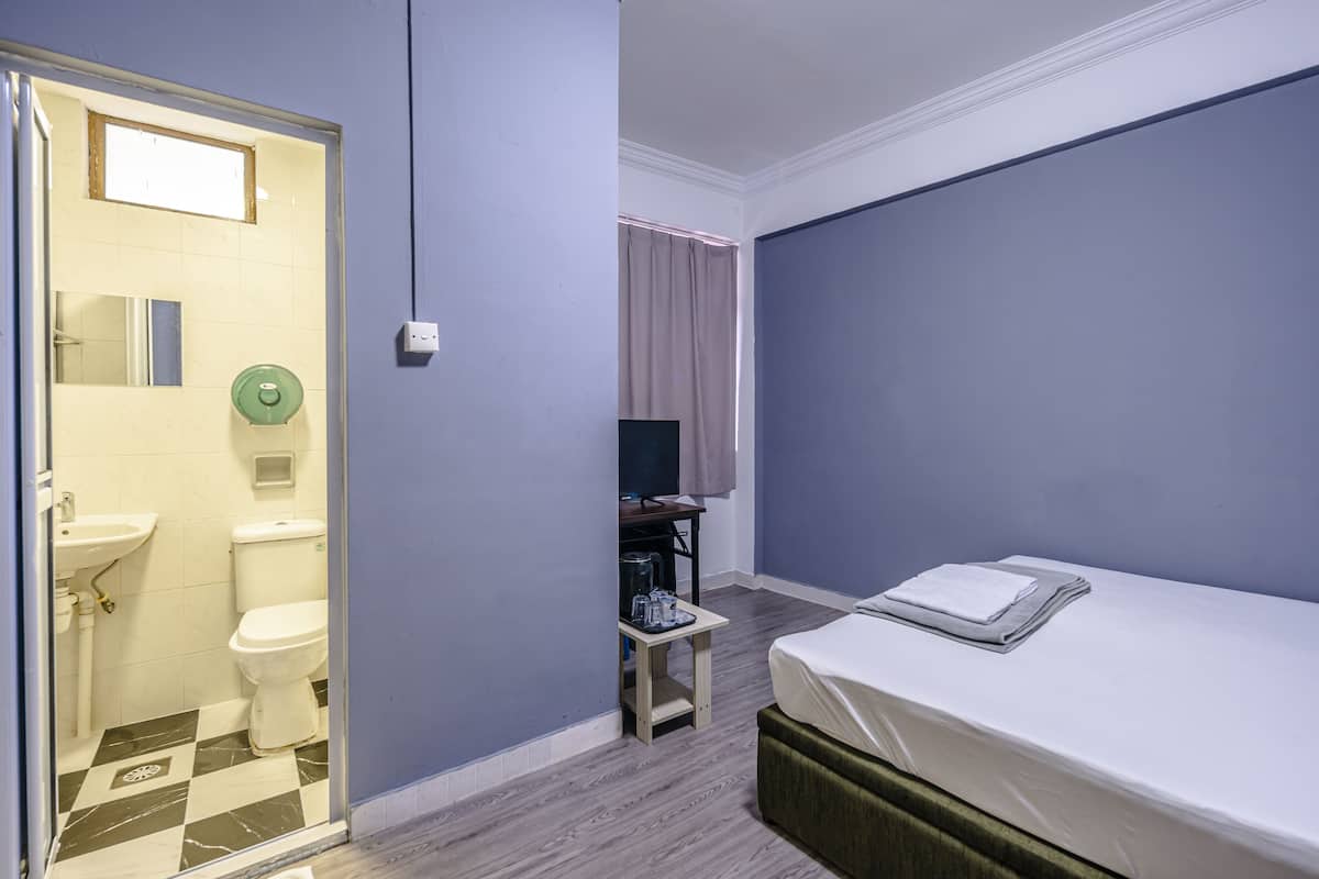 A hotel room with a bed, a small table with a TV, a bathroom with a toilet and sink, and a window with curtains.