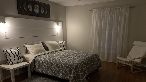 A bedroom with a bed, nightstands, a chair, a rug, and a wall-mounted light fixture. - Amazing home for 6 ! (Charlotte)