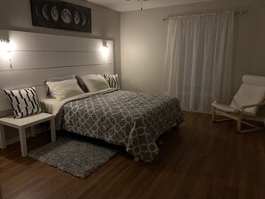 Ein Schlafzimmer mit Bett, Nachttischen, einem Sessel, einem Teppich und einer Wandleuchte.