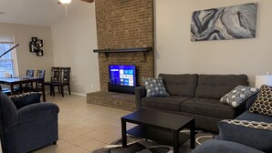 A living room with a brick fireplace, a flat-screen TV, a sofa, and a coffee table. - Amazing home for 6 ! (Charlotte)