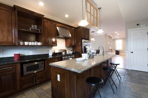 A spacious kitchen with dark wood cabinets, a granite countertop, stainless steel appliances, and a central island with bar stools. - Gorgeous designer home in Capital Hill (Washington)