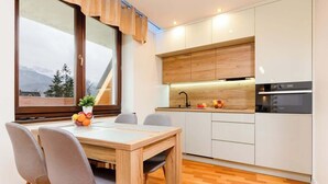 A modern kitchen with wooden cabinets, a built-in oven, and a dining area with a table and chairs. - Suite with Mountain View | Gym | Sauna. (Koscielisko)