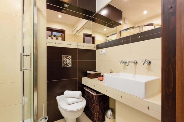 A modern bathroom with a glass shower enclosure, a white toilet, a large white sink, and dark tiled walls. - Suite with Mountain View | Gym | Sauna. (Koscielisko)