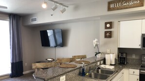 A modern kitchen with granite countertops, a flat-screen TV, a coffee maker, and a "Hello Sunshine" sign.