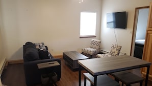 Een woonkamer met een bank, fauteuils, een salontafel en een eettafel met stoelen.