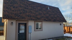 Een gelijkvloers huis met een donkerbruin shingle dak, een voordeur met een ruit, een klein raam en een brievenbus.