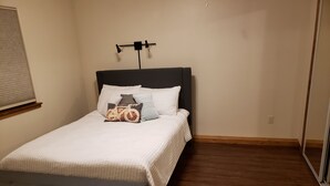 Een slaapkamer met een bed, een hoofdbord, een nachtkastje en een raam met zonwering.