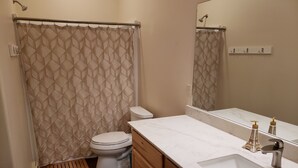 Een badkamer met toilet, douchegordijn, wastafelmeubel en houten kastjes.