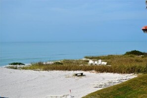 A beach with white sand, a few lounge chairs, and a small bench. - Beachcomber unit 207 (Longboat Key)