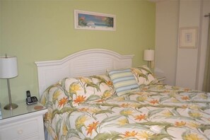 A bed with floral bedding, a bedside lamp, and a phone on a nightstand. - Beachcomber unit 207 (Longboat Key)