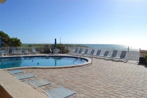 A pool area with lounge chairs and a view of the ocean.