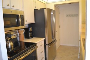 A compact kitchen with stainless steel appliances, including a microwave, oven, and refrigerator, with a sign reading "BEACH GEAR" on the wall.