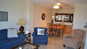 A living room with a sofa, armchair, coffee table, and a dining area with a table and chairs. - Beachcomber unit 605 (Longboat Key)