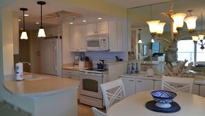 A modern kitchen with white cabinets, a microwave, stove, and a dining area with a table and chairs. - Beachcomber unit 302 (Longboat Key)