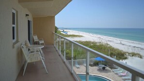 A balcony with white chairs and a pool, overlooking a beach with sand and water. - Beachcomber unit 302 (Longboat Key)