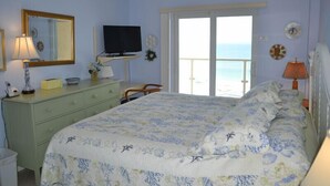 A bedroom with a bed, dresser, television, and a view of the sea through a sliding door. - Beachcomber unit 302 (Longboat Key)