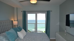 A bedroom with a bed, a TV, a dresser, and a view of the ocean. - Beachcomber unit 604 (Longboat Key)