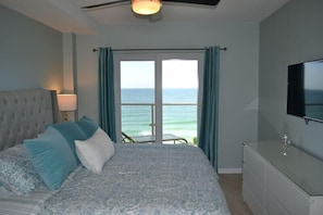 A bedroom with a bed, a TV, a dresser, and a view of the ocean.