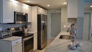 A modern kitchen with white cabinets, stainless steel appliances, a marble countertop, and a decorative seahorse sculpture. - Beachcomber unit 604 (Longboat Key)