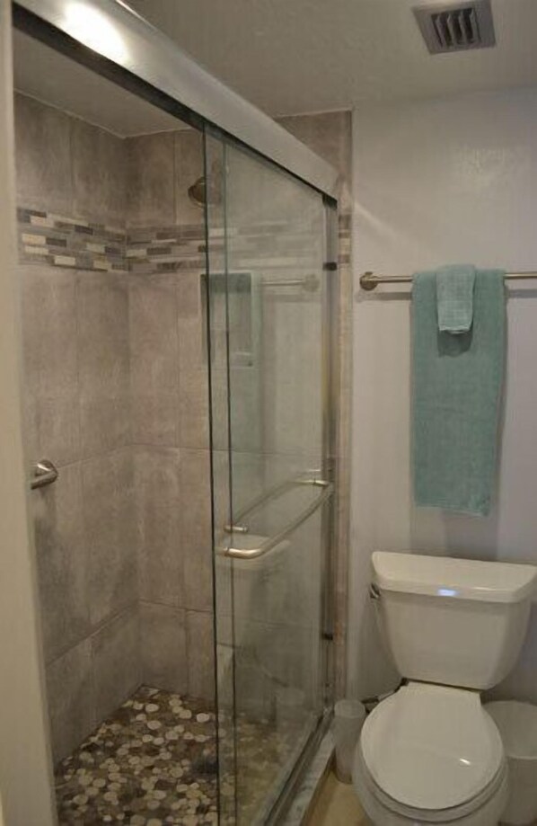 A bathroom with a glass-enclosed shower, a toilet, and a towel rack. - Beachcomber unit 604 (Longboat Key)