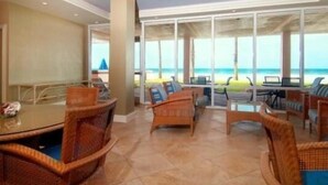 A spacious indoor area with a large glass wall offering a view of the beach. There are wicker chairs and a round table with chairs. - Beachcomber unit 604 (Longboat Key)