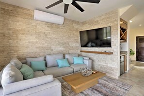 A modern living room with a grey sofa, teal cushions, a wooden coffee table, and a flat-screen TV mounted on a stone wall.