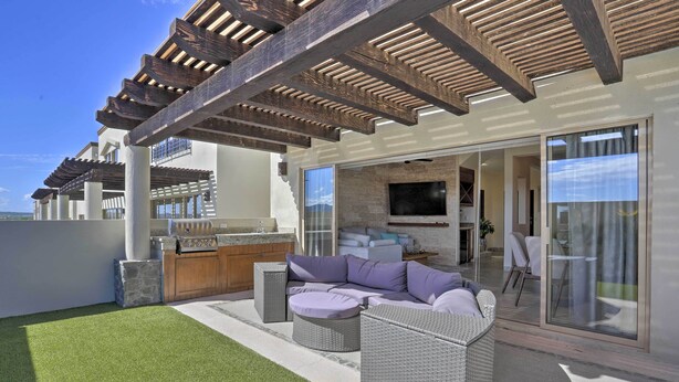 Un'area relax esterna moderna, con barbecue integrato, ampio spazio salotto imbottito e struttura a pergola.