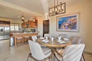 A modern kitchen with a central island, bar stools, and a dining table set for six.