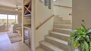 Una scala con ringhiera in legno, un angolo cottura con piano di lavoro e mobili, e un soggiorno con divano e tavolino.