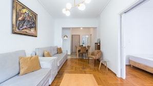 Een moderne woonkamer met een bank, een eettafel en een stoel. Aan de muur hangt een schilderij en er is een plafondlamp.