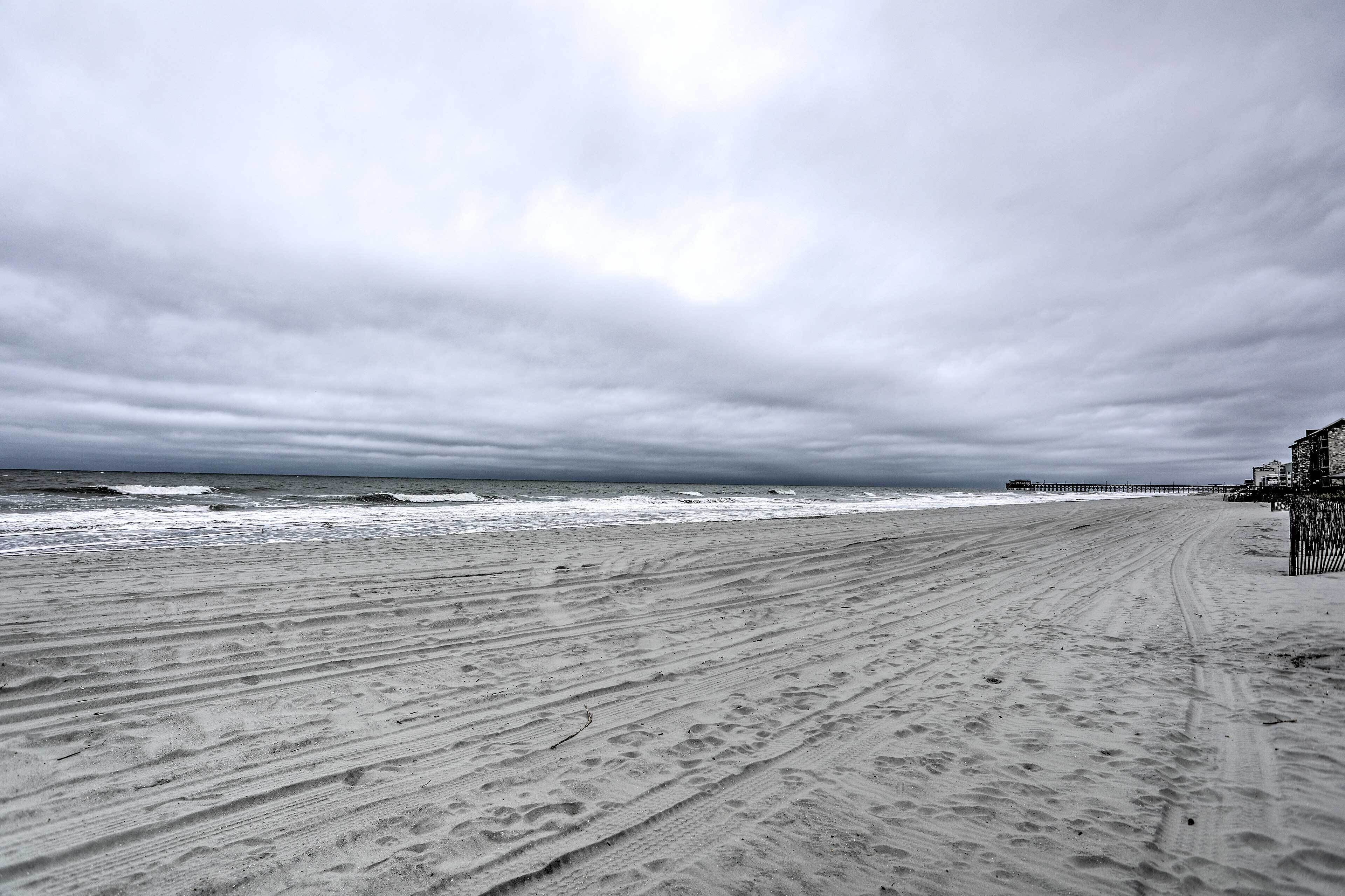 Une plage avec une jetée qui s’avance dans l’océan, une plage de sable et un ciel nuageux.