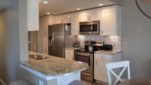 A modern kitchen with white cabinets, stainless steel appliances, a granite countertop, and a patterned backsplash. - Beachcomber unit 502 (Longboat Key)