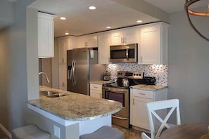 A modern kitchen with white cabinets, stainless steel appliances, a granite countertop, and a patterned backsplash. - Beachcomber unit 502 (Longboat Key)