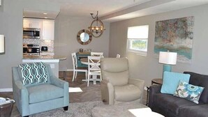 A modern living room with a dining area, a kitchen in the background, and a large painting on the wall. - Beachcomber unit 502 (Longboat Key)