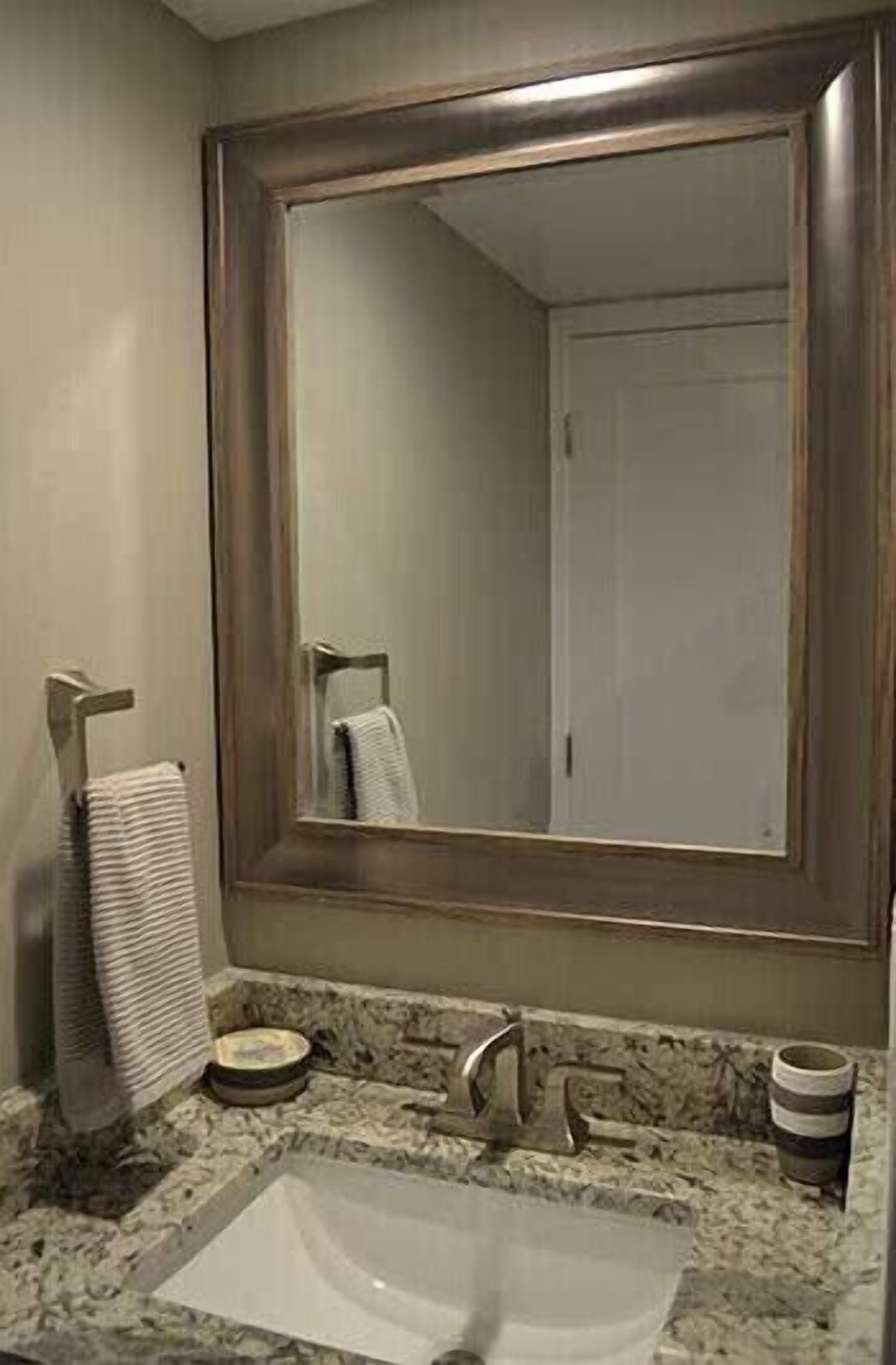 A bathroom with a large mirror, a sink, a towel rack, and a cup.