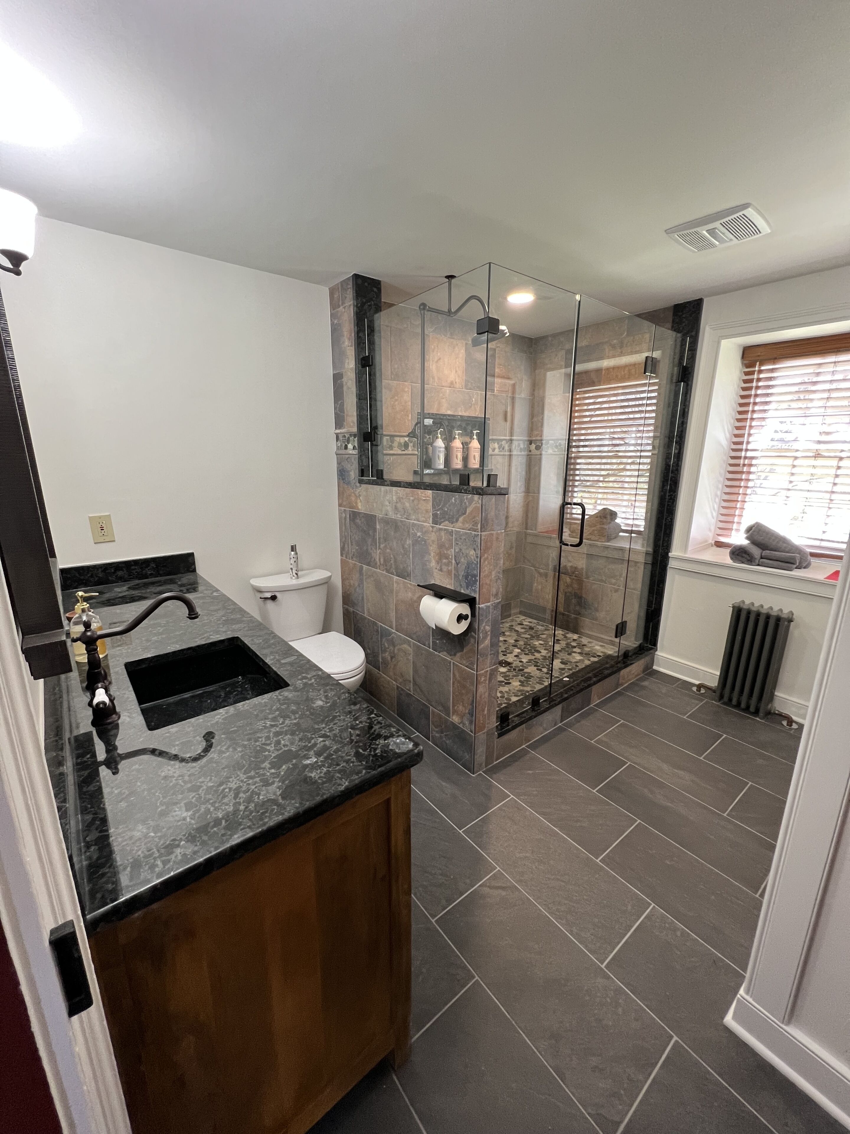 Un baño moderno con cabina de ducha de vidrio, lavamanos de mármol negro y un inodoro.