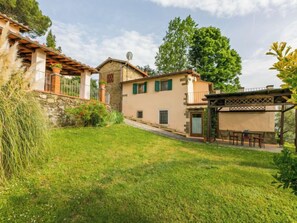 A traditional stone house with a sloped roof, a small garden, and a pergola with outdoor seating.