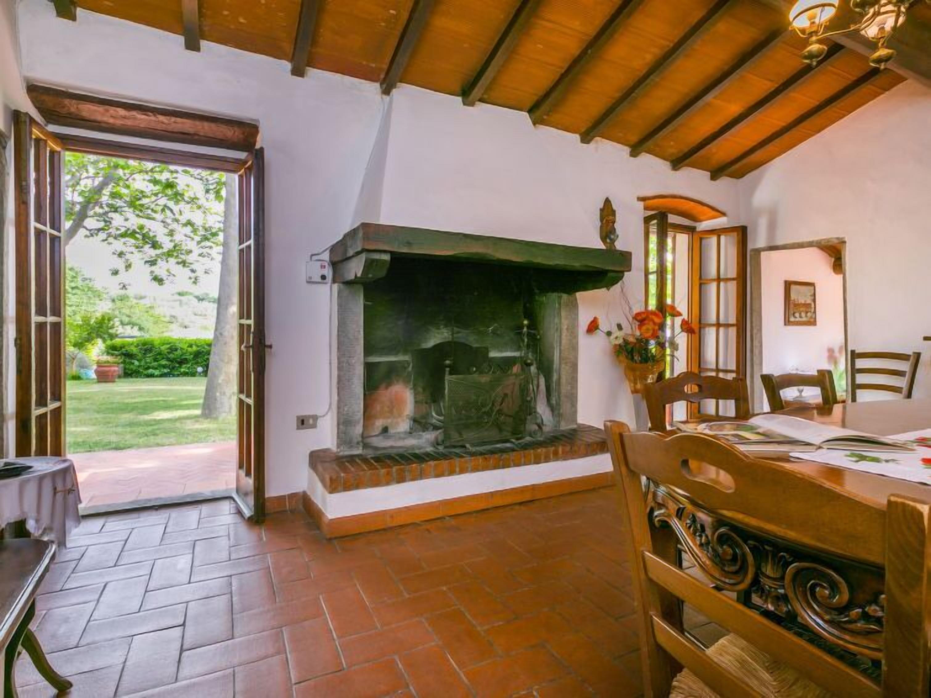 Una habitación acogedora con chimenea, una mesa de comedor con sillas y vistas al jardín a través de un ventanal abierto.
